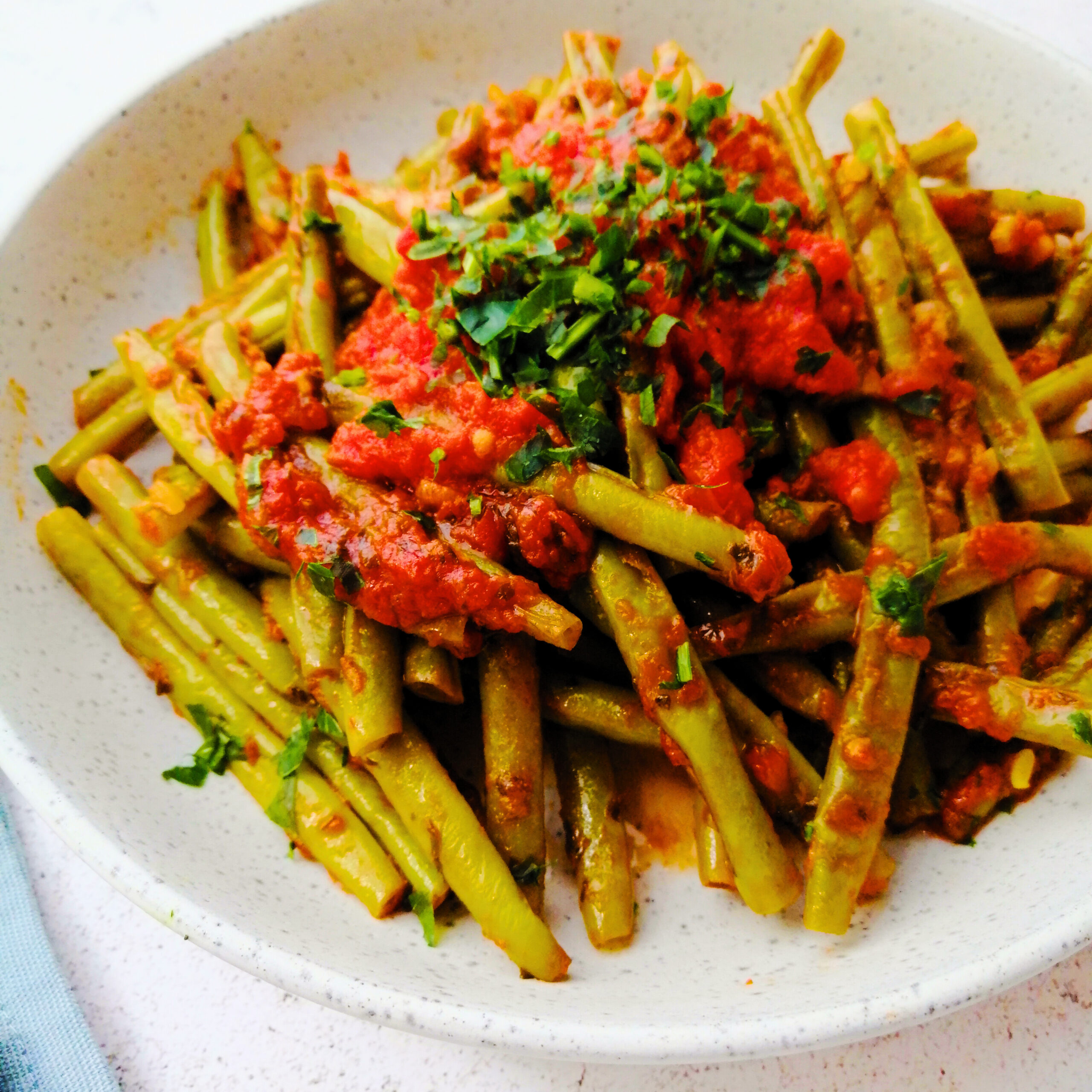 Bowl of green beans cooked in s a tomato sauce with sprinkled chopped parsley