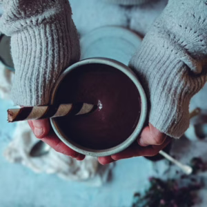 Hands of a person holding a ceramic mug filled with hot chocolate and a wafer twirl