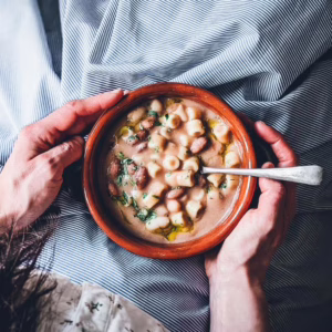 Shot from above of a woman eating pasta e fagioli from a terracotta bowl she is holding