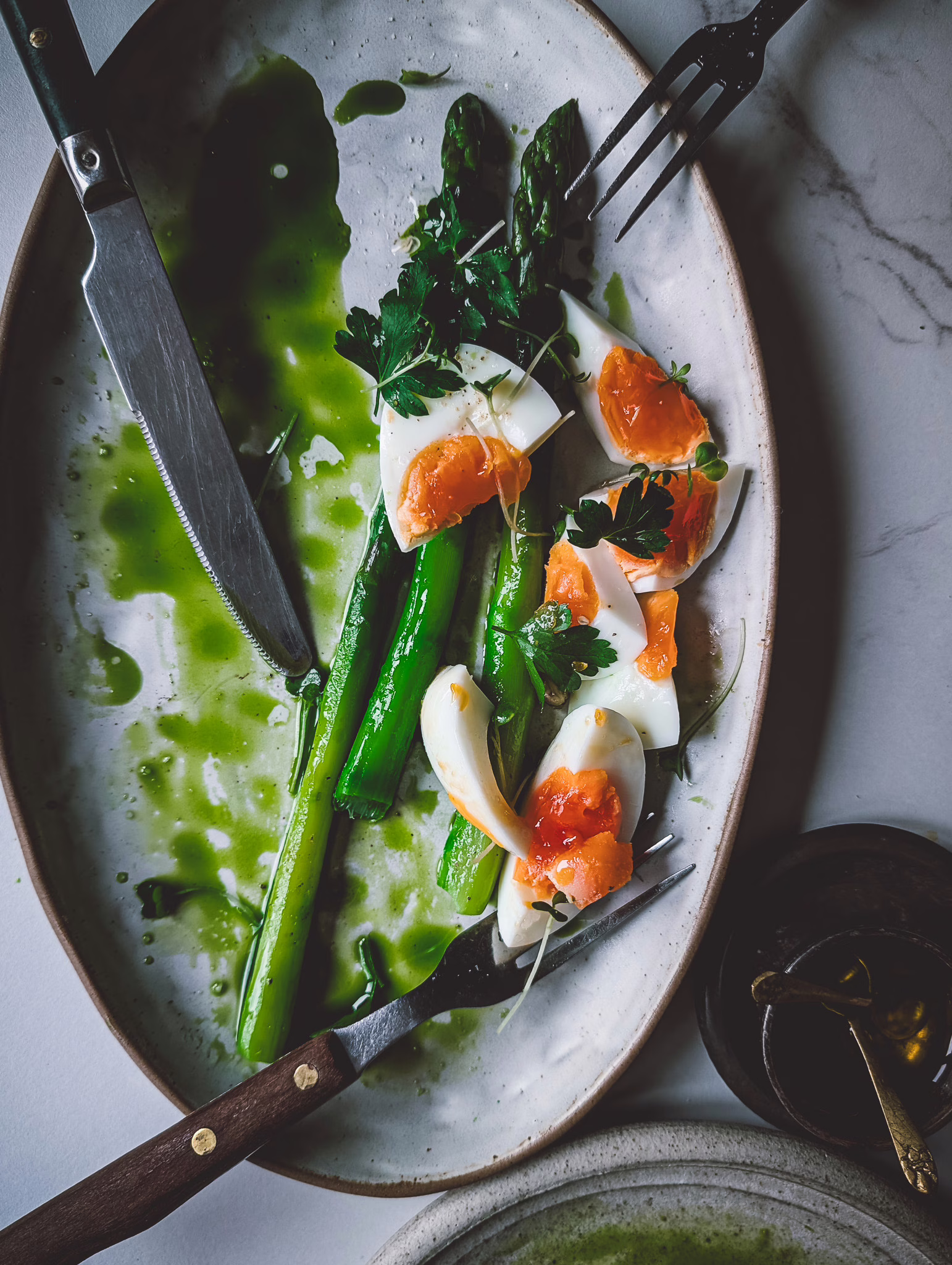 Close up of asparagus and eggs serving plate half empty. Some vintage wooden cutlery is also on the plate.