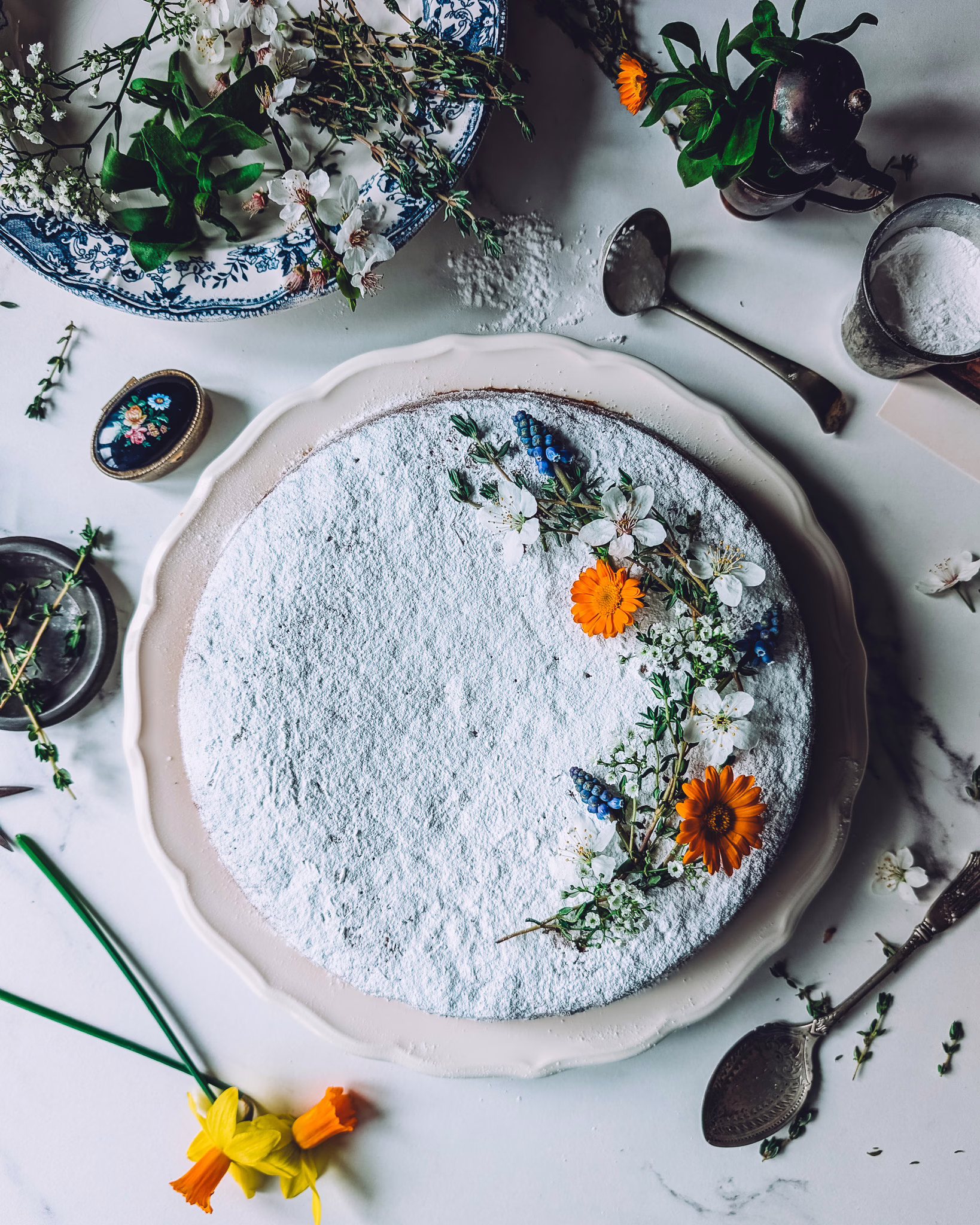 Italian carrot cake dusted with icing sugar and decorated with orange, white and blue edible flowers and thyme sprigs