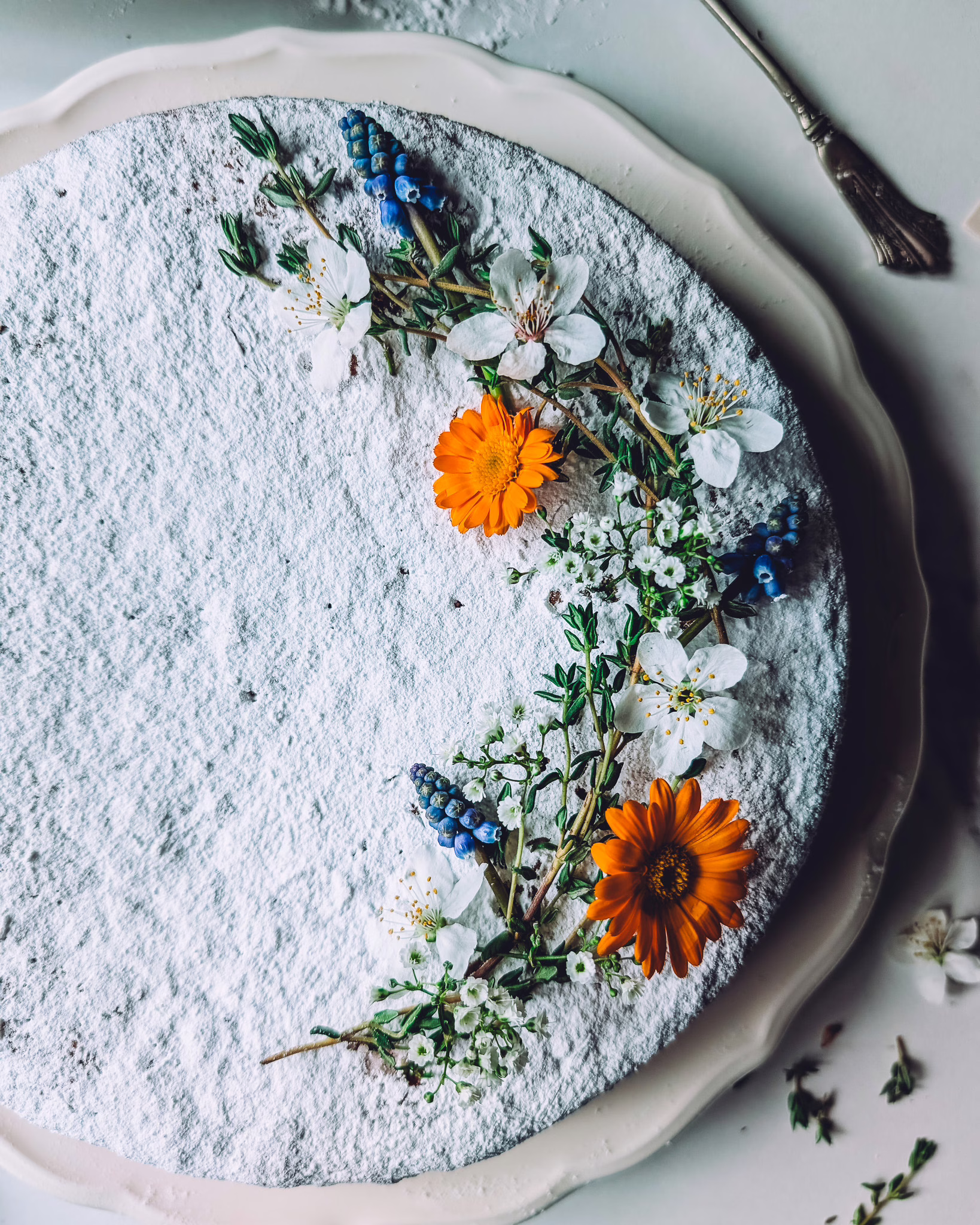 Italian carrot cake dusted with icing sugar and decorated with orange, white and blue edible flowers and thyme sprigs
