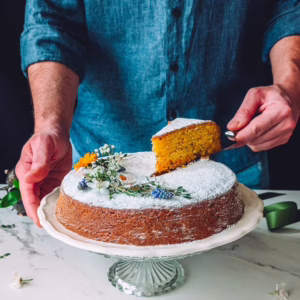 Man wearing blue shirt lifting a slice of carrot cake placed on a cake stand