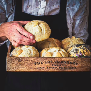 Woman holding a rosetta bread roll and a tray of other rolls.