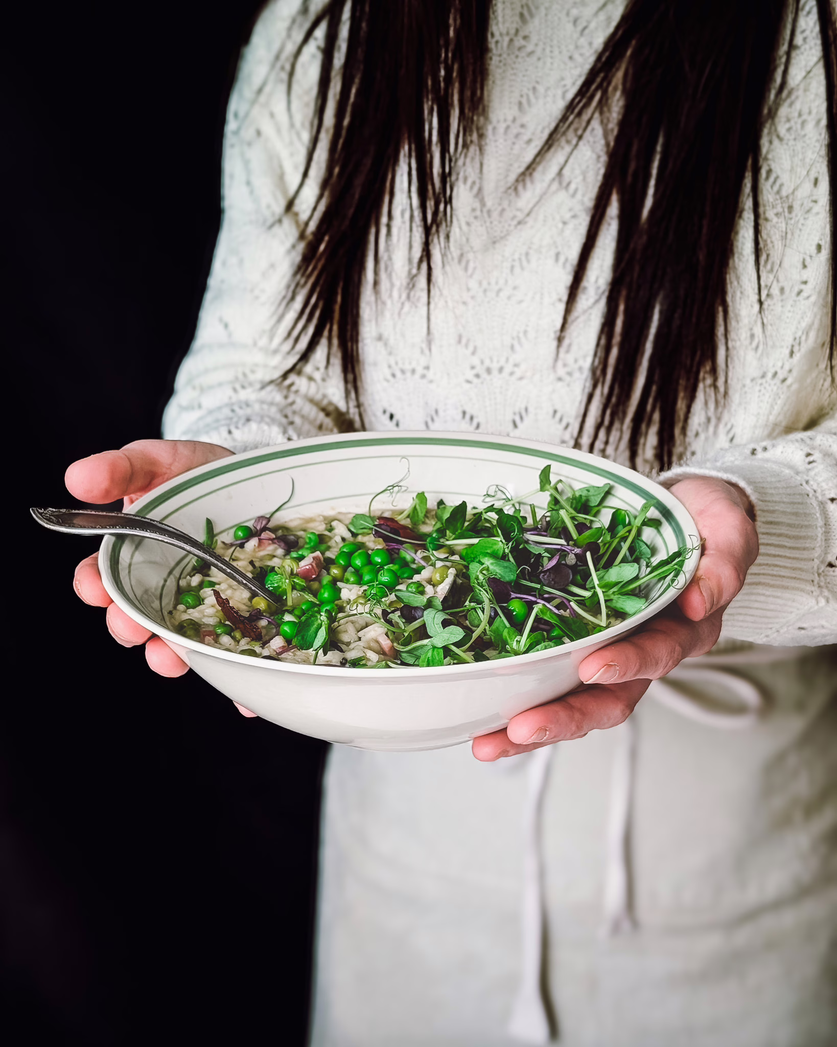 Person wearing white knitwear top and white apron holding a bowl of rice and peas