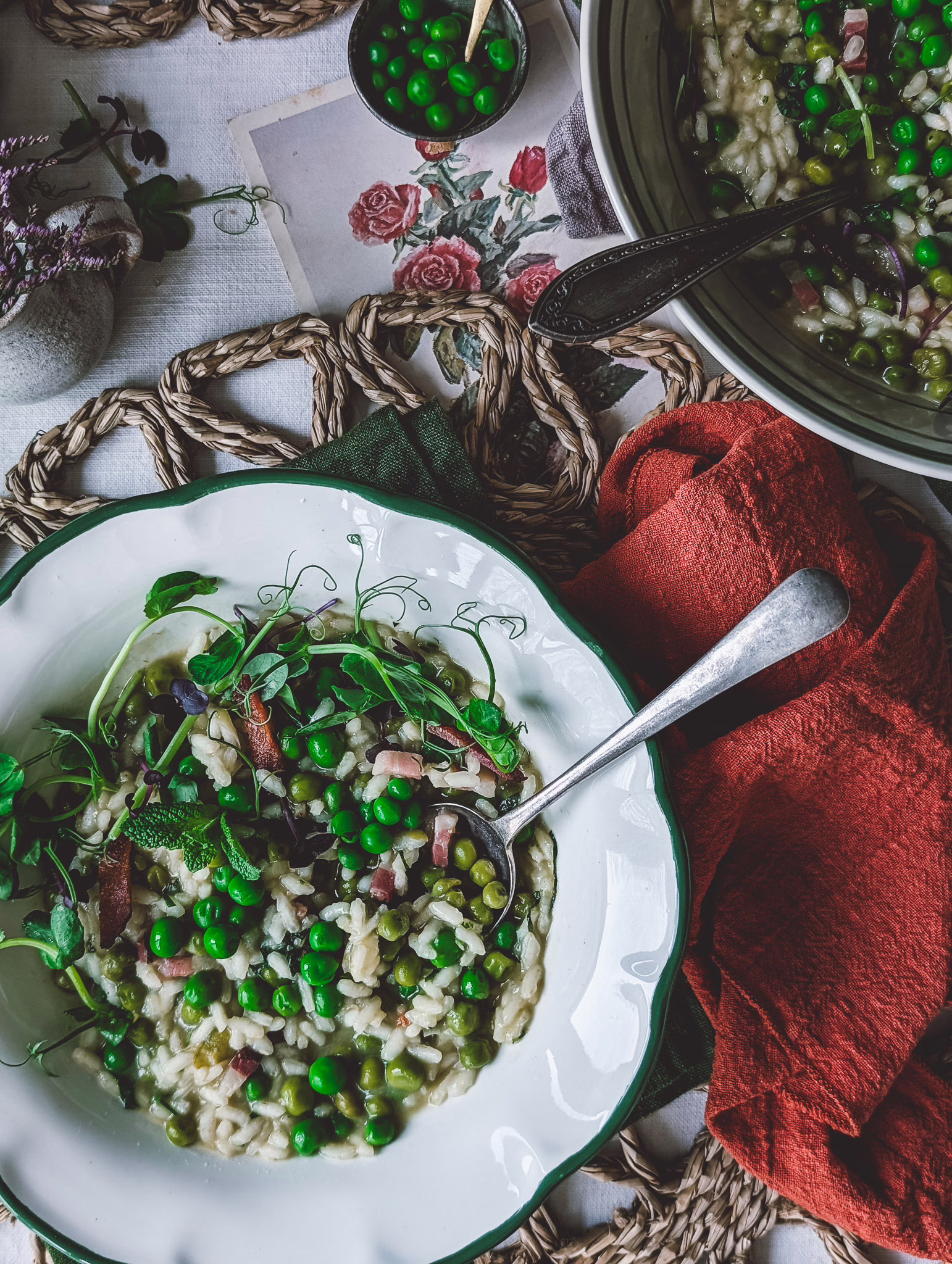 Serving bowl with rice and peas, and two bowls of rice and peas on a table. A ladle is coming out of the serving bowl, which is surrounded by terracotta napkings. The plates and the table are decorated with pea shoots.