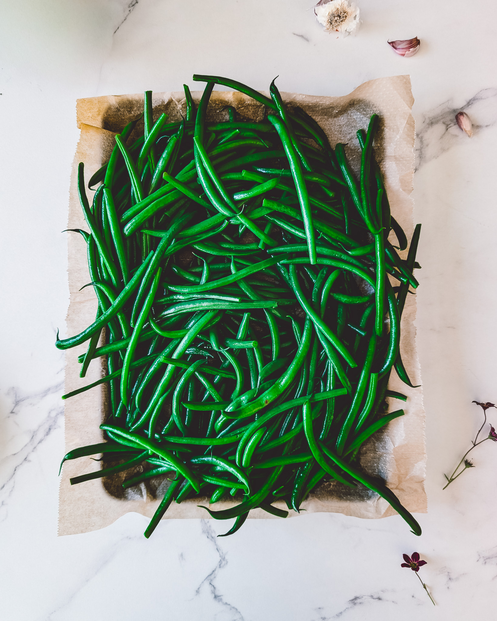 Cooked green beans on a sheet of baking paper, surrounded by little purple flowers