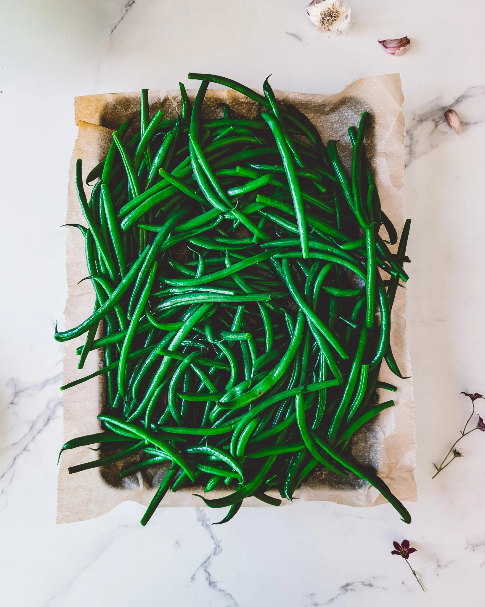 Cooked green beans on a sheet of baking paper, surrounded by little purple flowers