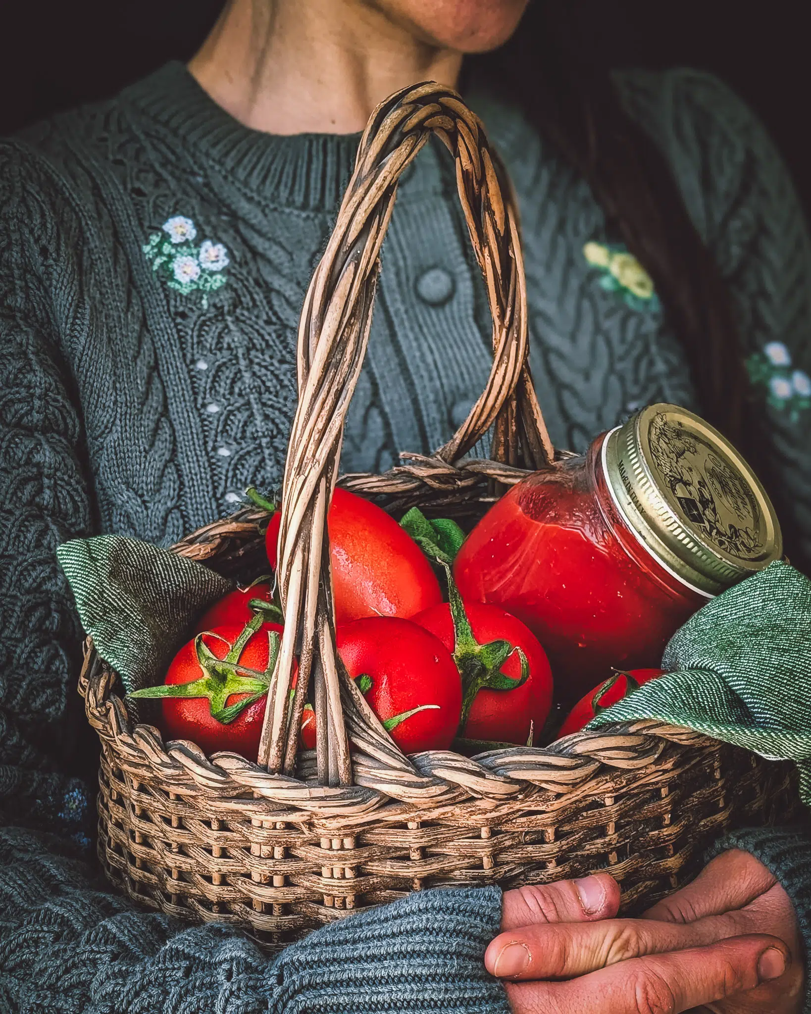 Person carrying a basket full of tomatoes and a tomato glass jar.