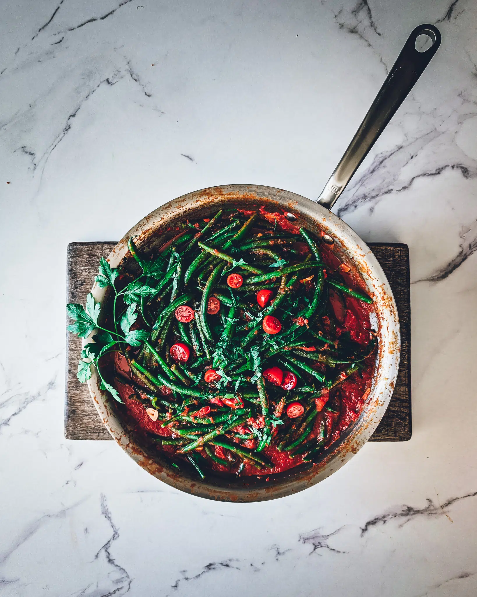 Pan with green beans in garlicky tomato sauce on a wooden chopping board