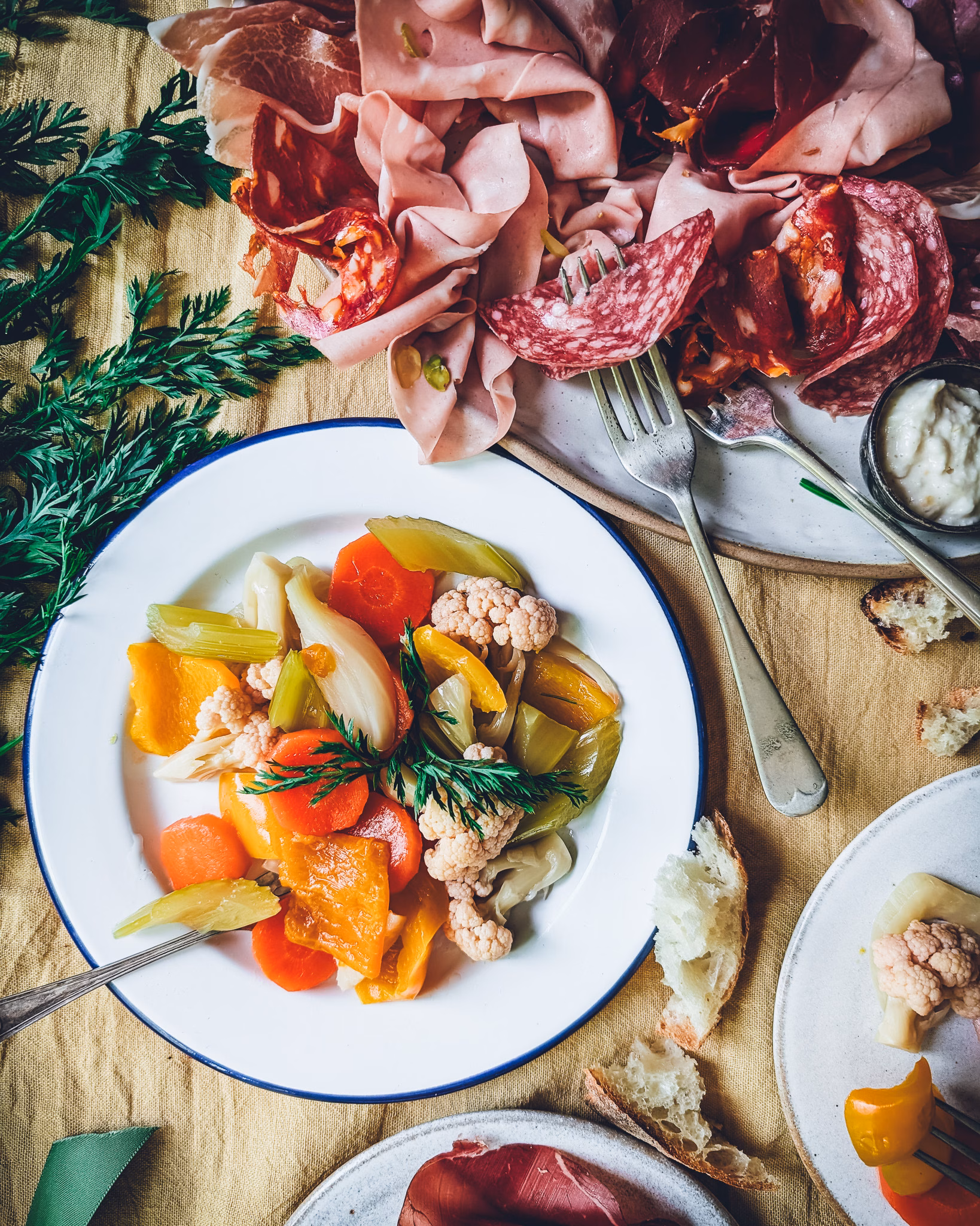 Giardiniera Italian pickled vegetables served with charcuterie, herbs, and wine in a flat lay composition.