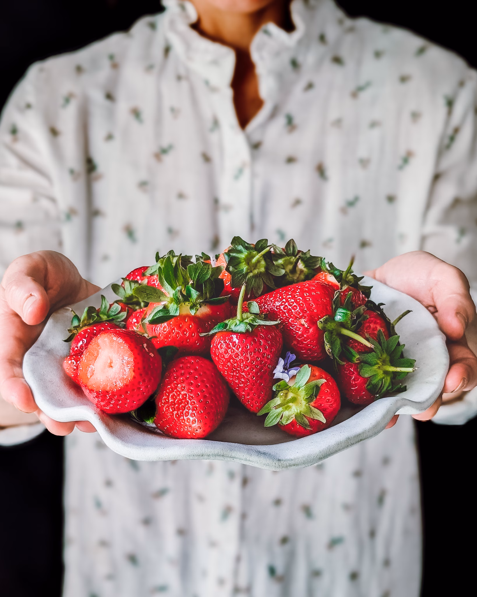 Woman holding plate full of beautiful fresh strawberries