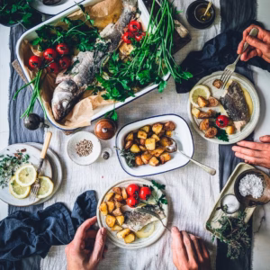 Table with tray of sea bass and roasted potatoes, alongside plates full of roasted potatoes, cherry tomatoes, and sea bass slices