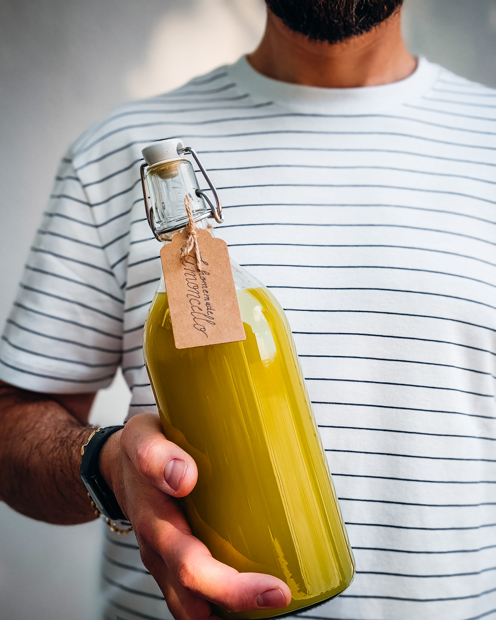 Man wearing white striped t-shirt and holding a bottle of homemade limoncello