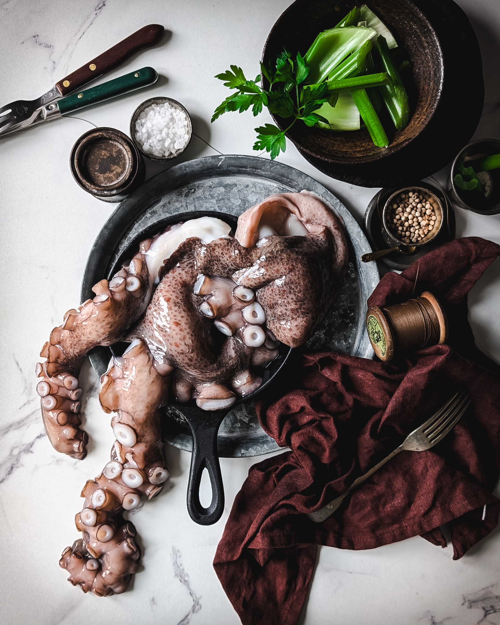 Raw octopus on a table surrounded by a napkin, some celery, and cutlery