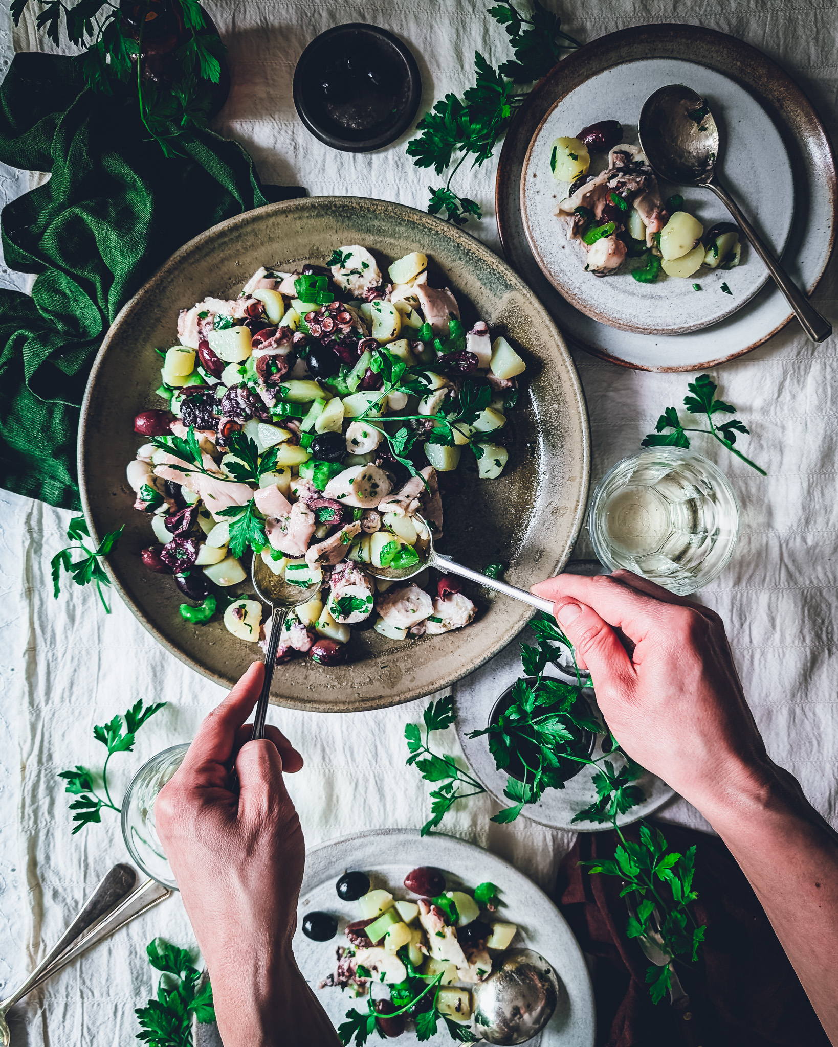 Colourful octopus and potato salad plates and bowls on a table. A person is serving the salada.
