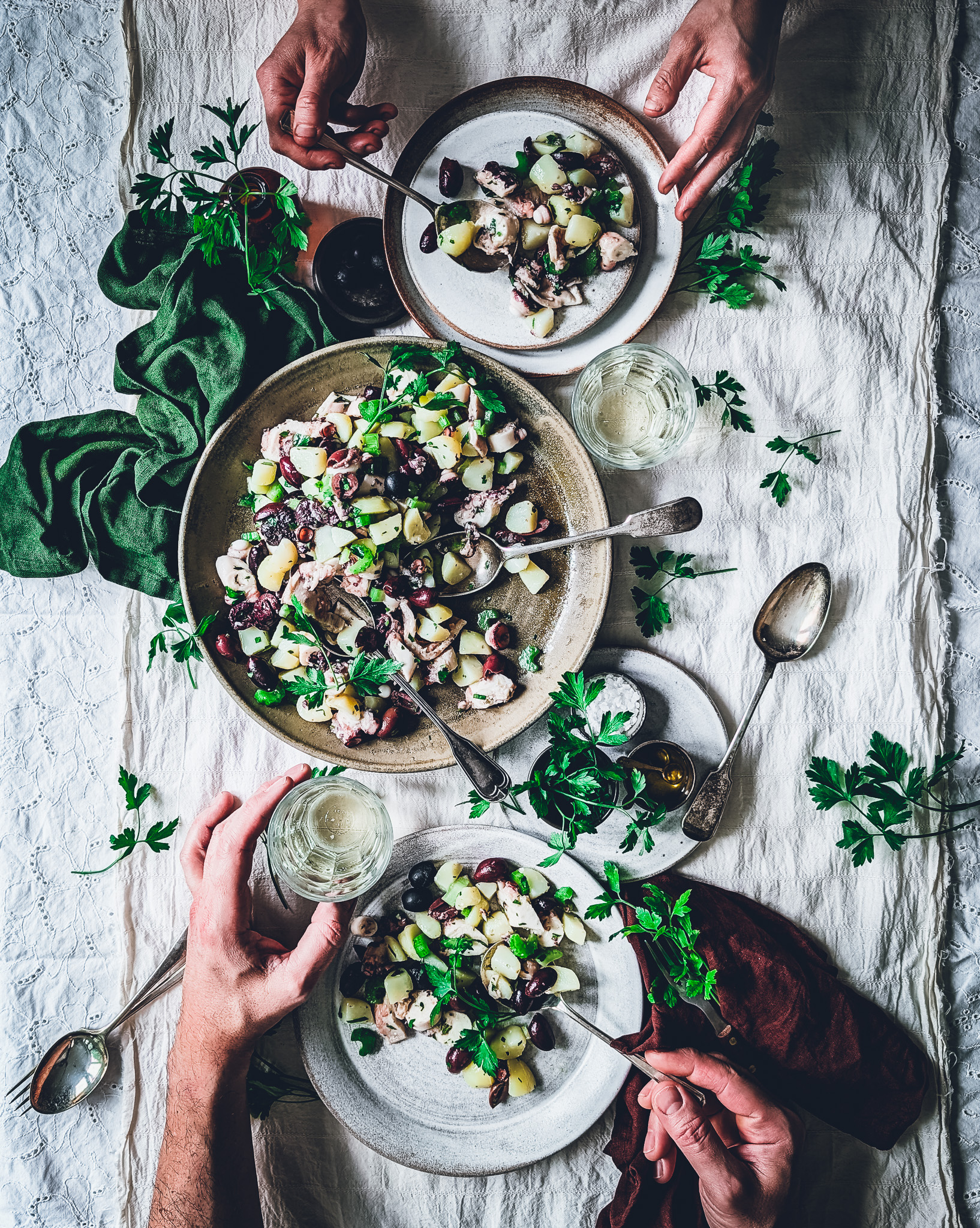 hands of two people sitting at a table and eating octopus and potato salad from a serving plate