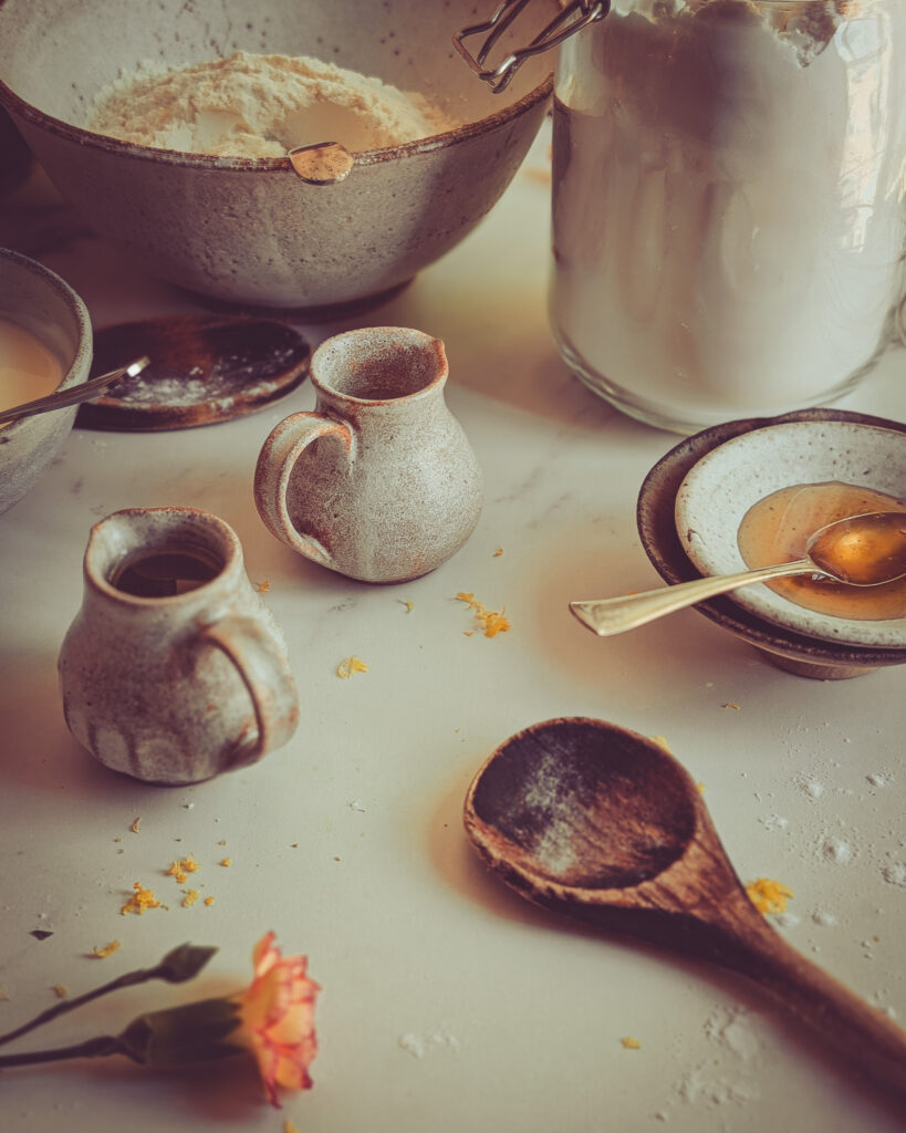 Close up of cake ingredients including a wooden spoon, flavour and two small jugs