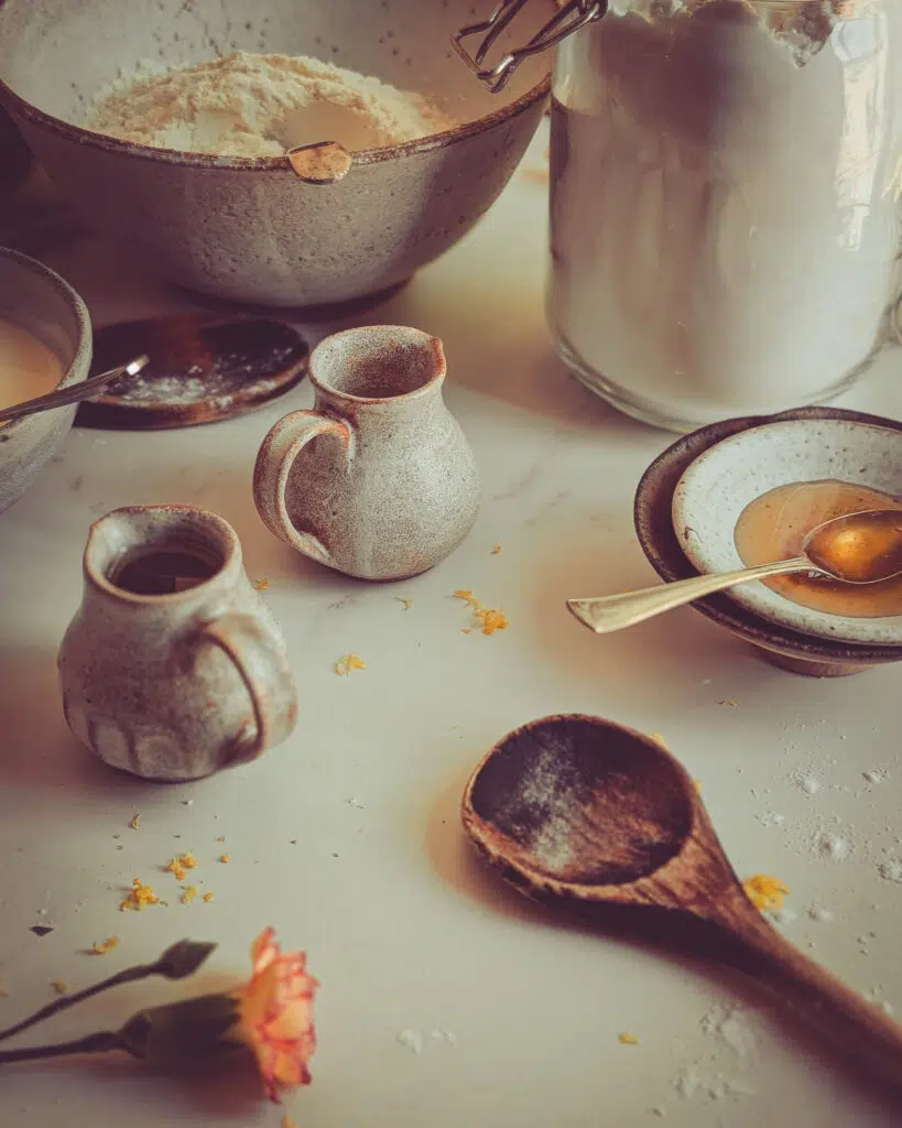 Close up of cake ingredients including a wooden spoon, flavour and two small jugs
