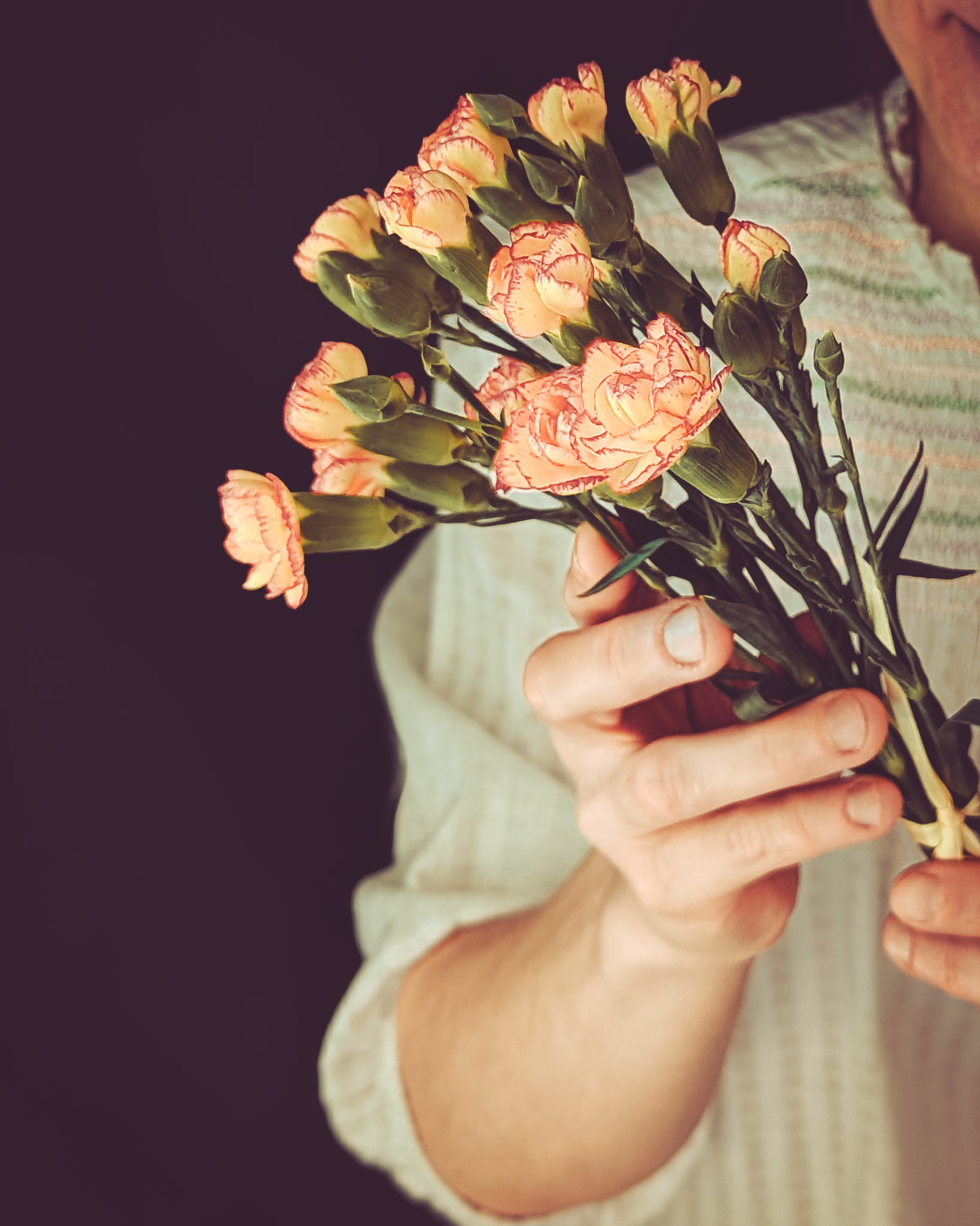 Woman holding bunch of light pink and yellow flowers.