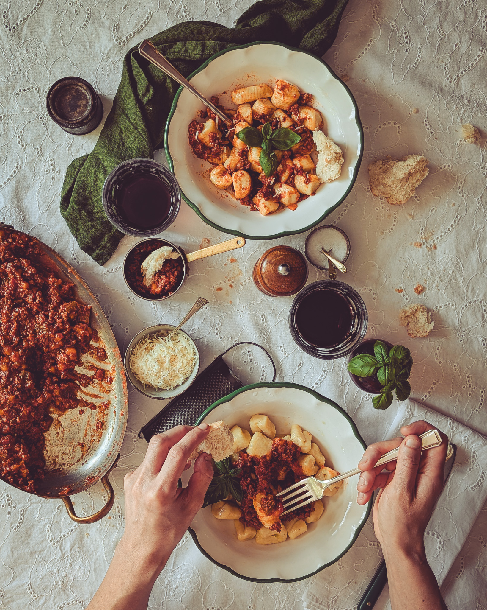 Table with two plates full of gnocchi al ragu. A person is eating from one of the plates.