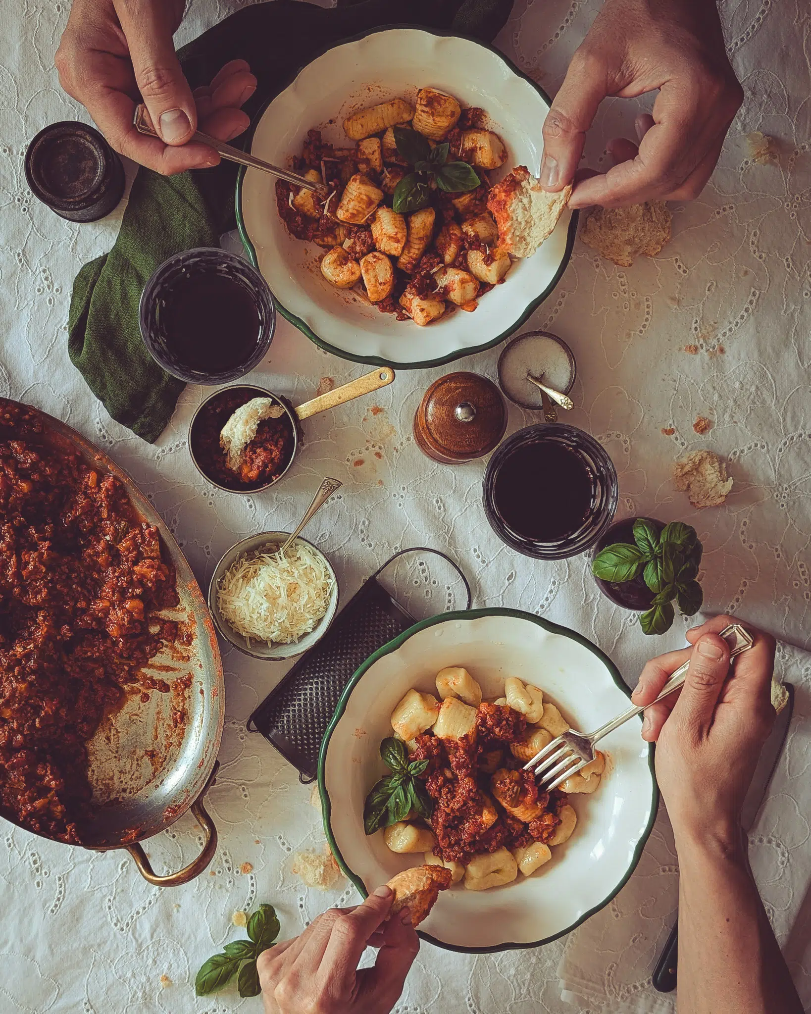 Two people sitting at a dressed table and eating from two plates of gnocchi al ragu.