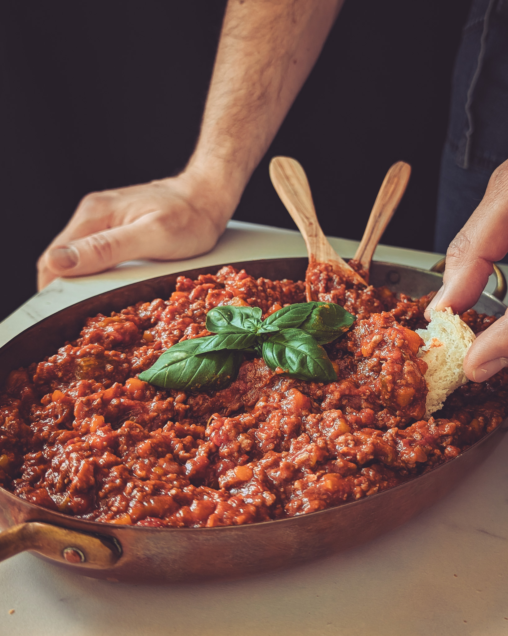 Hands of man eating ragu from a pot using bread.
