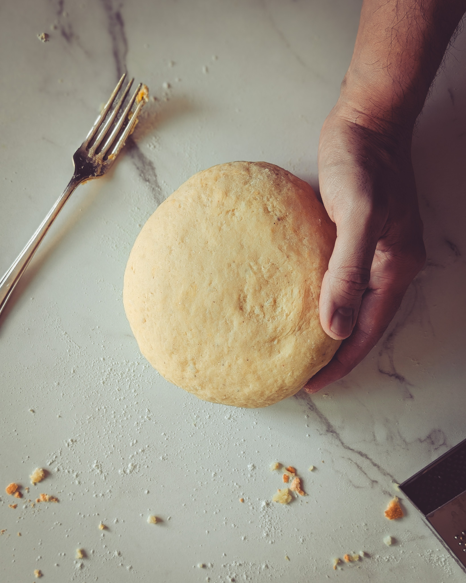 Hand of man holding dough of gnocchi on a marble table next to a dirty fork used to mix the dough.