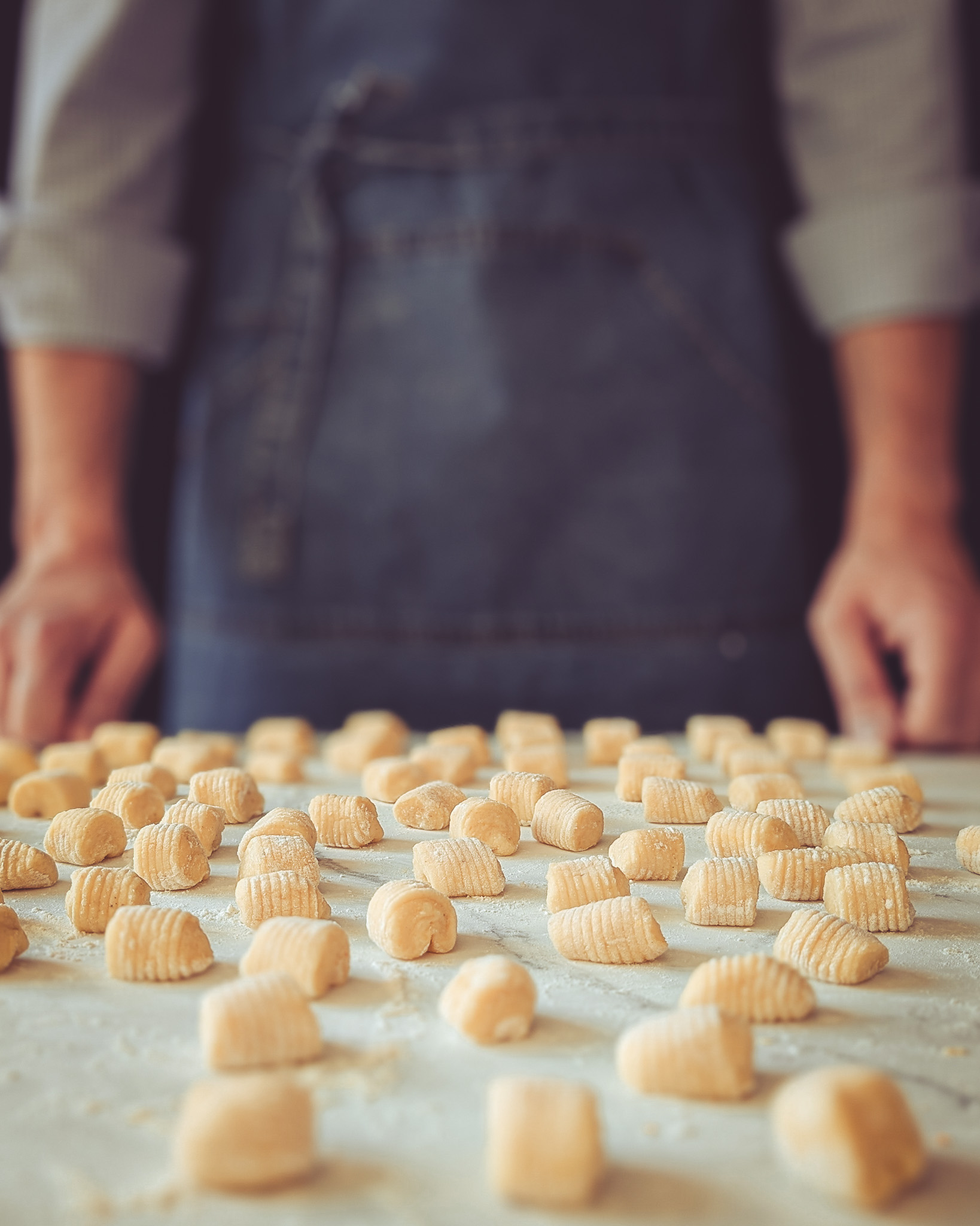 Man standing in front of a marble table full of raw gnocchi.