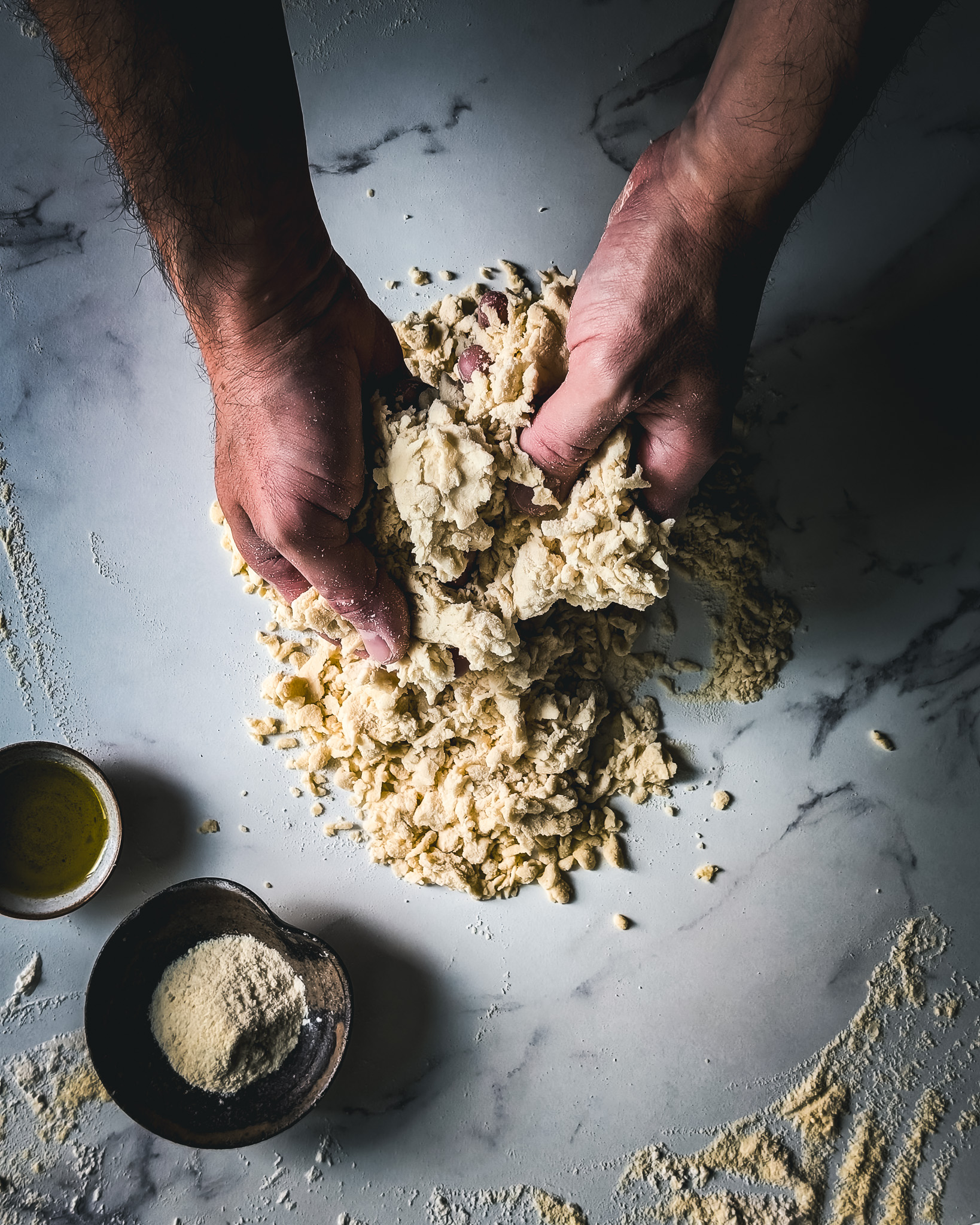 Hands of man mixing pasta dough on a marble table.