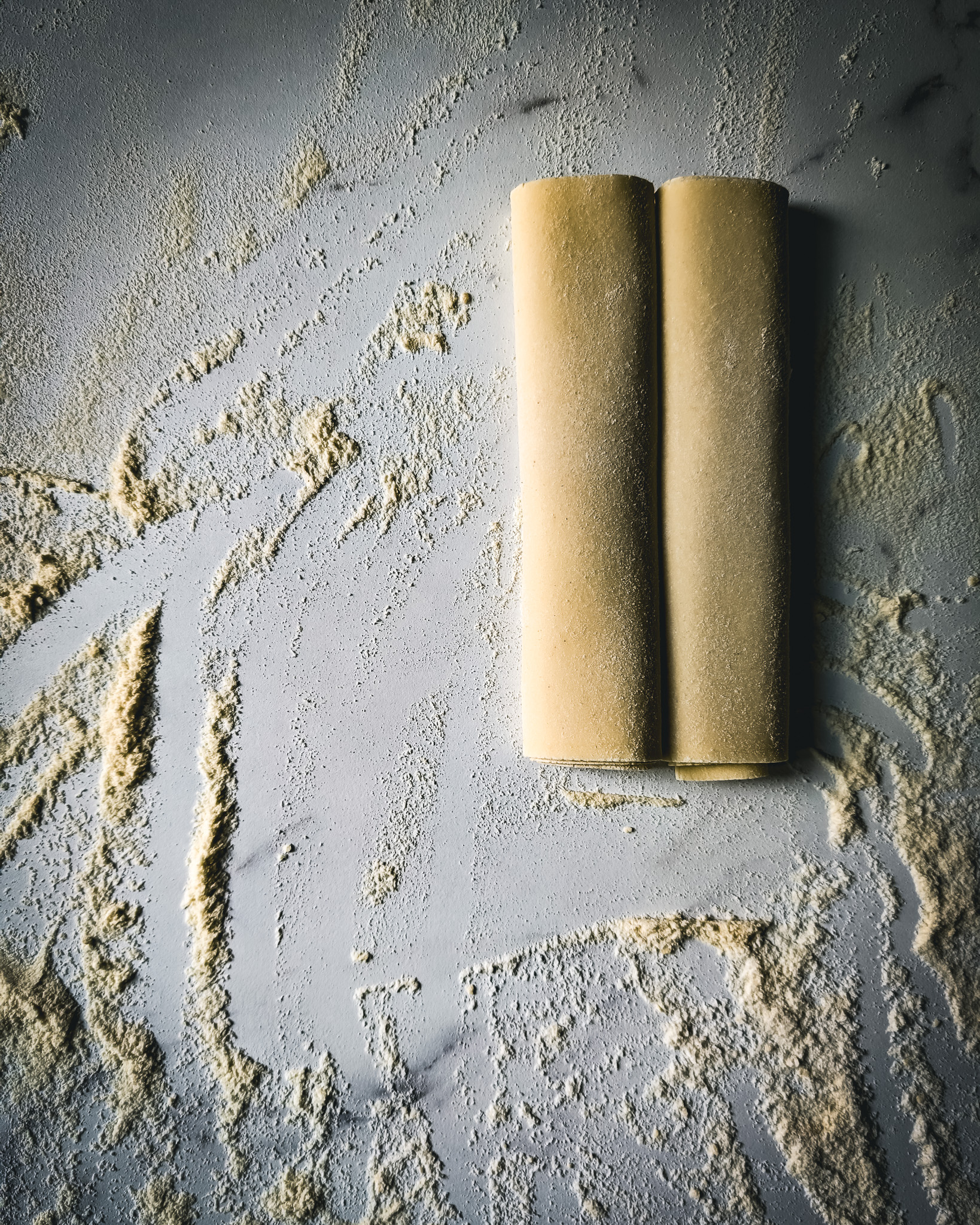 Sheet of fresh pasta rolled up on a marble table full of flour.