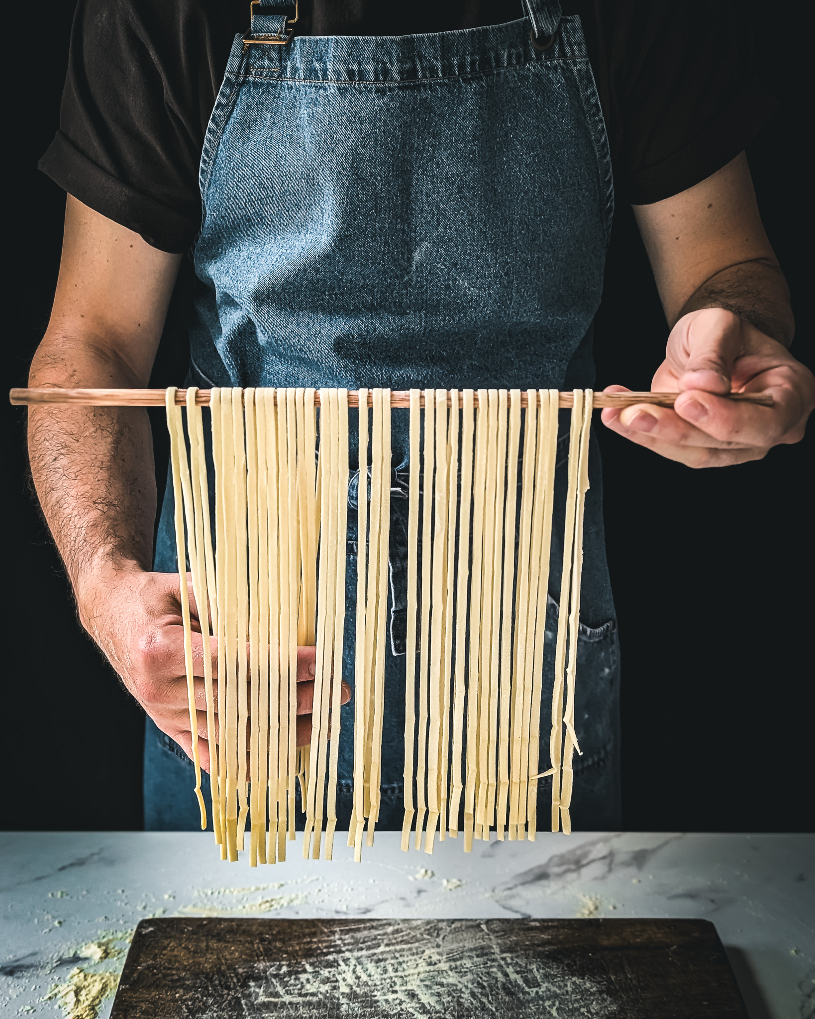 Hands of man lifting fresh linguine using a wooden stick.