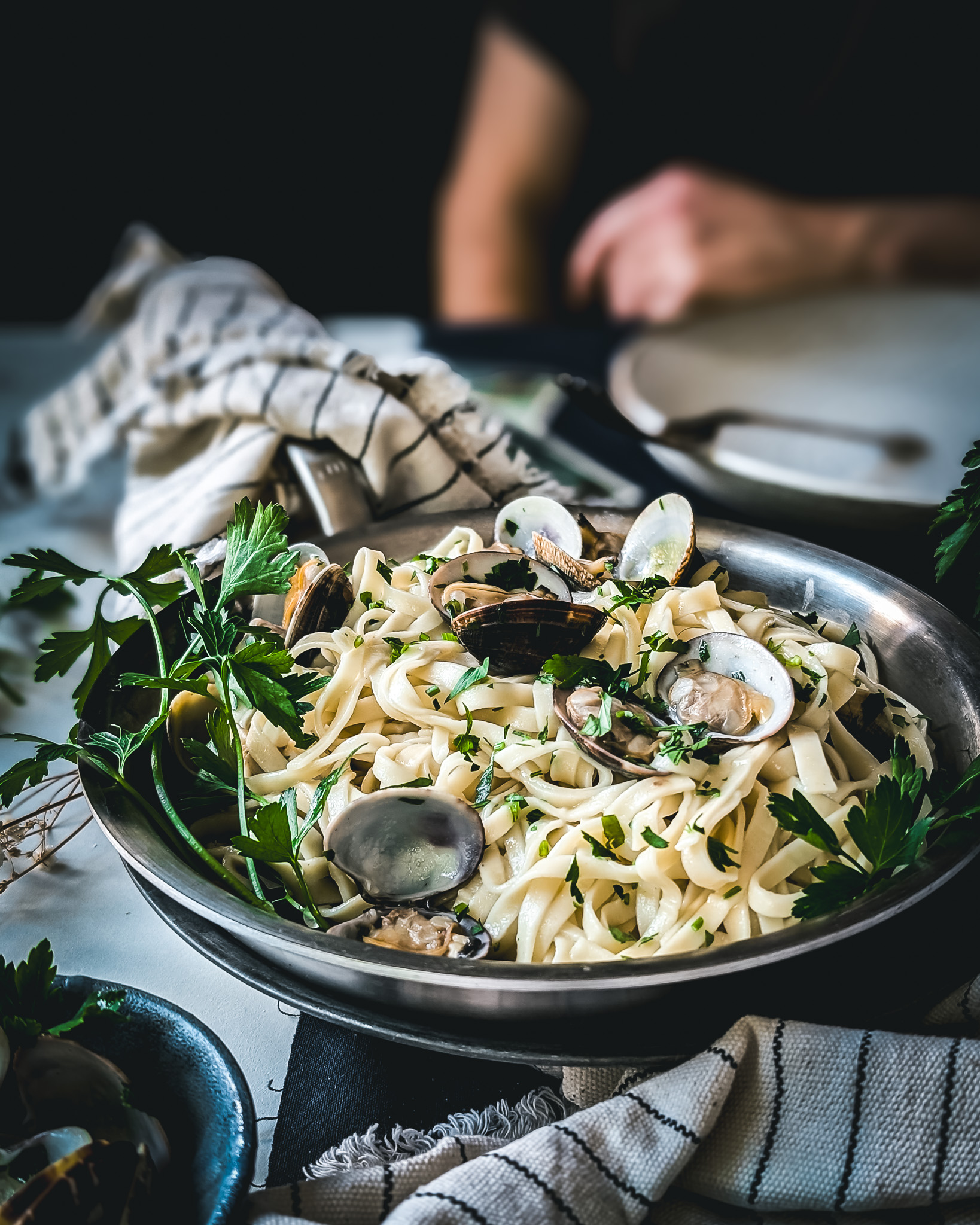 Pan full of linguine alle vongole. On the background the silhouette of a man.