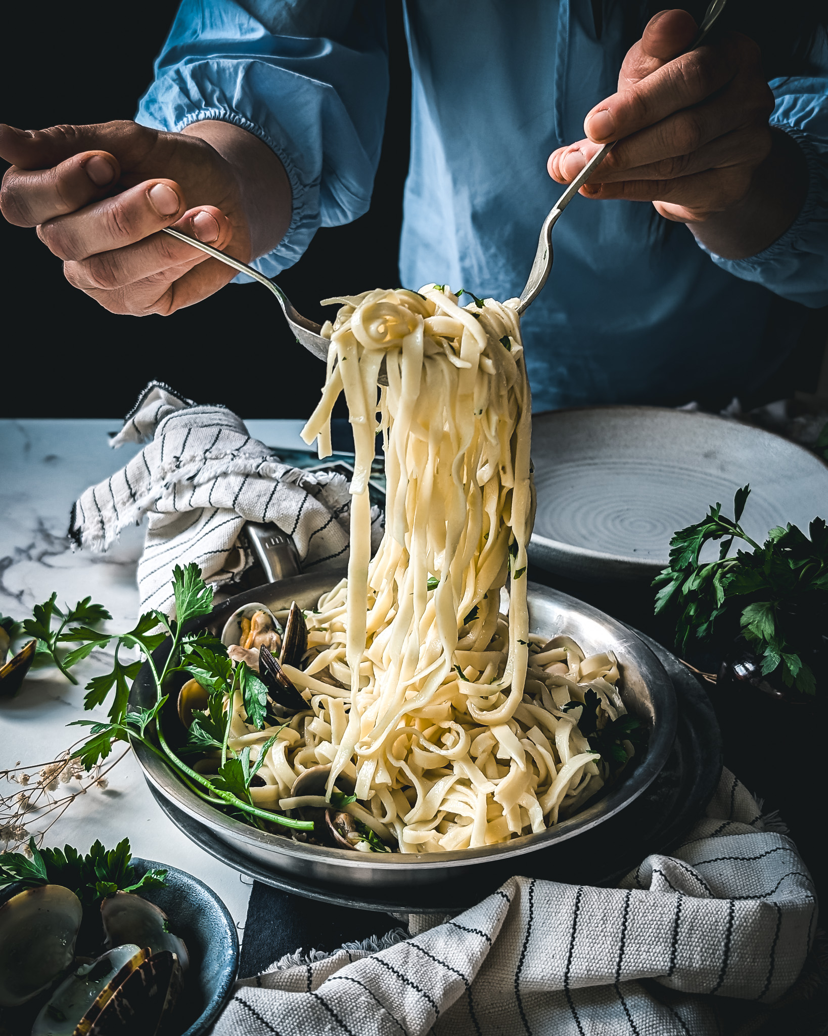 Person serving linguine alle vongole from a stainless stell pan.