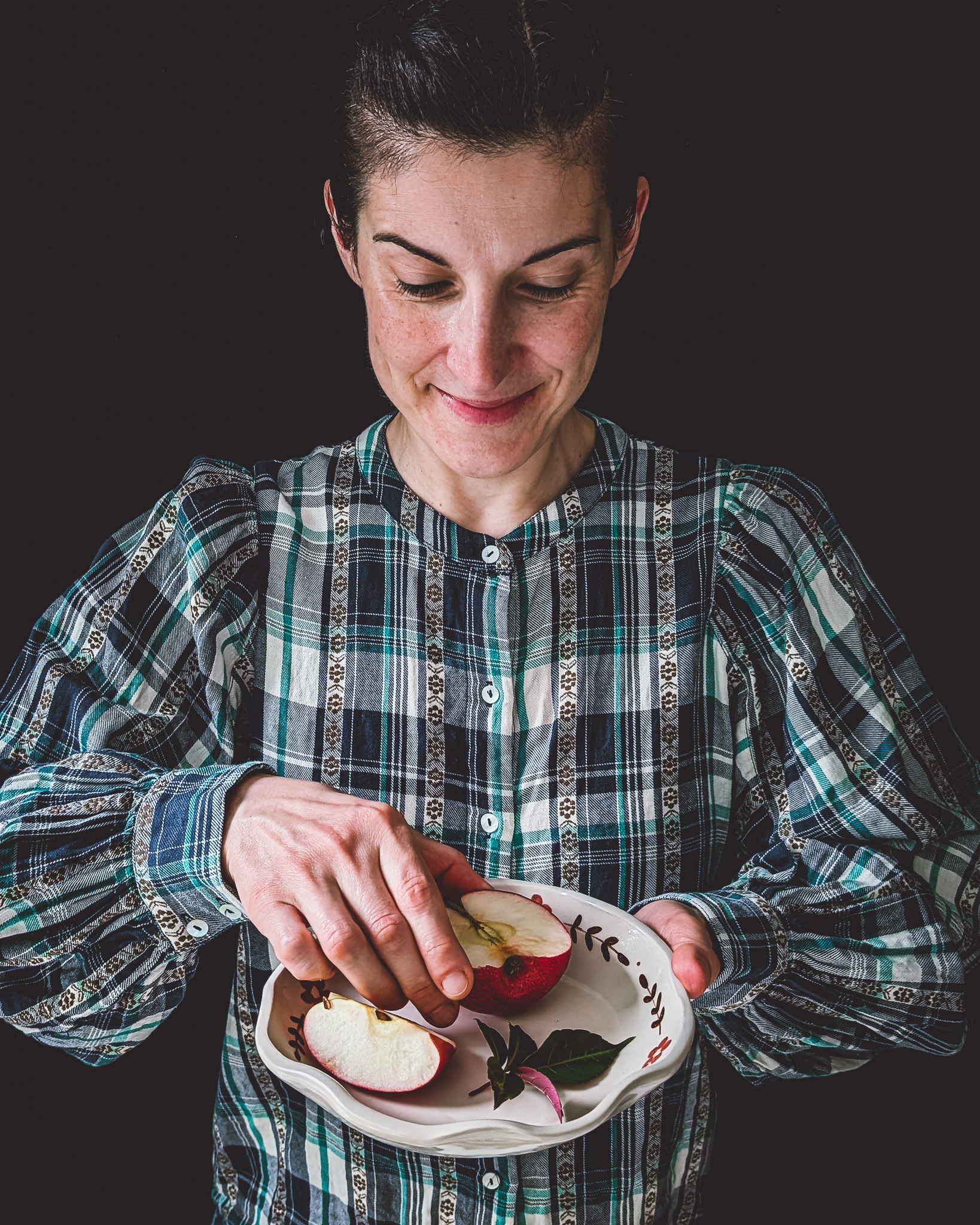 Woman holding plate with half an apple and a slice, and holding half the apple in one hand