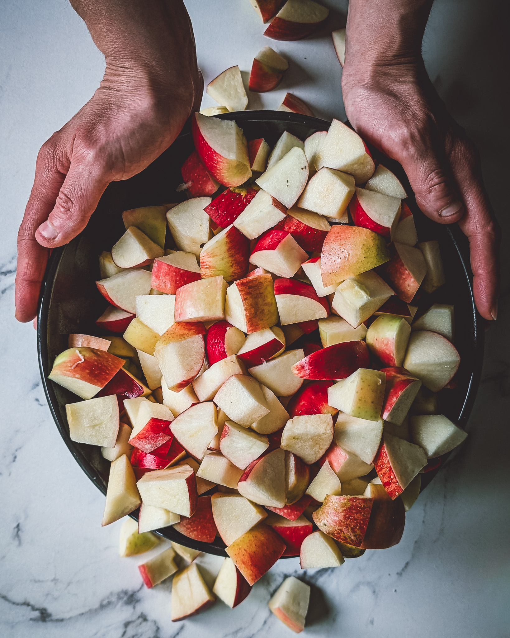 Two hands holding a bowl full of chopped apples.